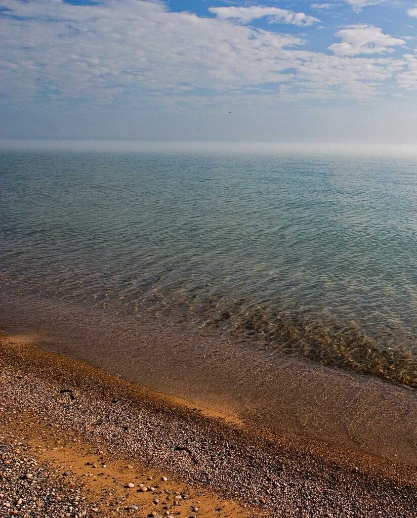 Blue, cloudy sky over a sandy shoreline and expanse of water.